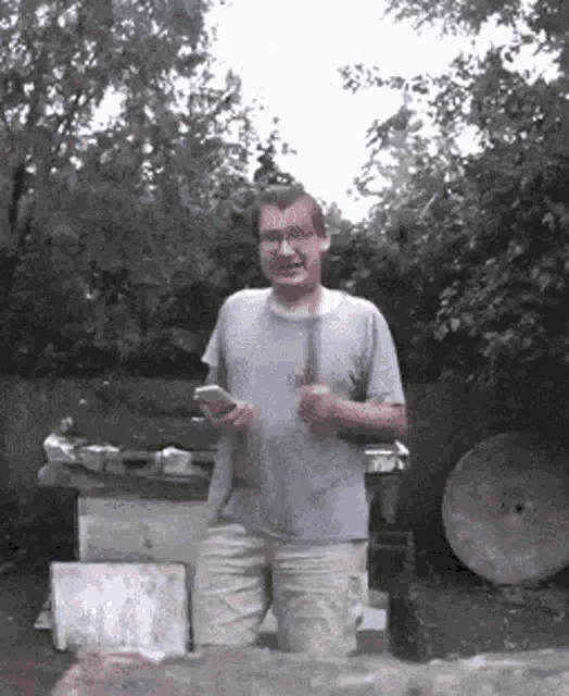 a man in a blue shirt is holding a hammer and looking at his cell phone .