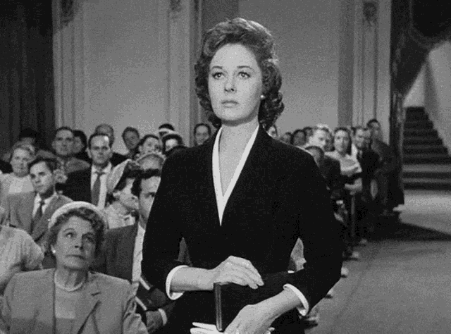 a woman stands in front of a crowd of people holding a bible