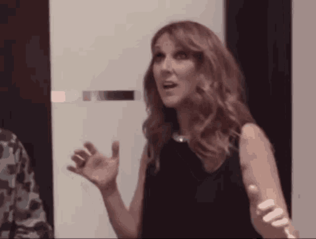 a woman in a black dress is standing in front of a door and talking to someone
