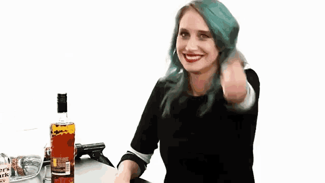 a woman with blue hair is sitting at a table with a bottle of whiskey