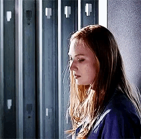 a girl with long hair is standing in front of a row of lockers .