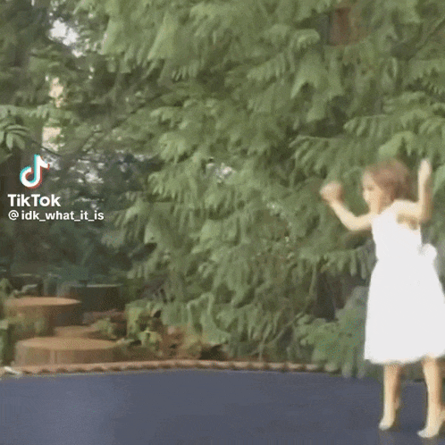 a little girl in a white dress is dancing on a trampoline ..
