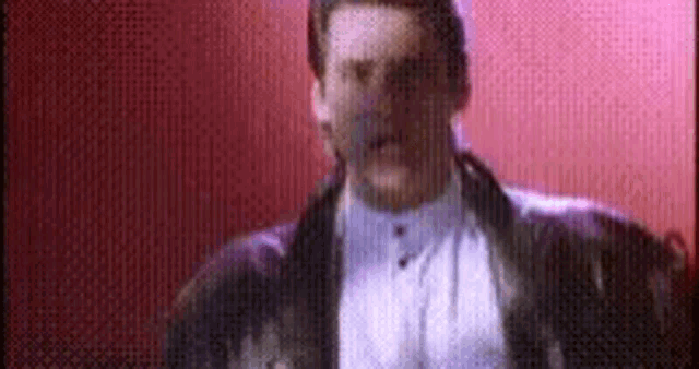 a man in a tuxedo and white shirt is standing in front of a pink wall .