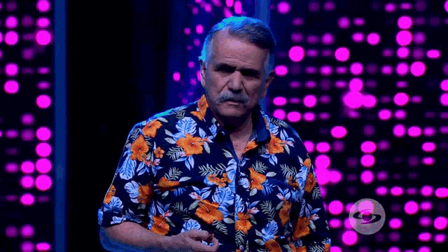 a man wearing a hawaiian shirt stands in front of a purple background