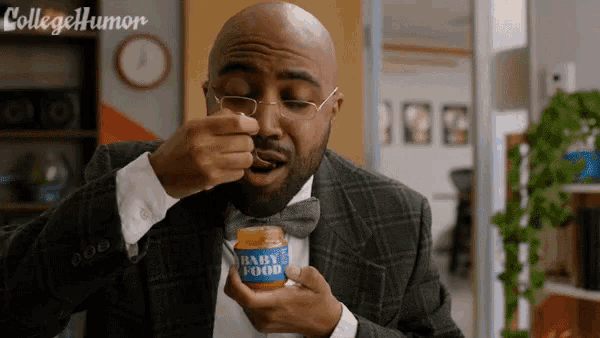 a man in a suit and bow tie is eating from a jar of baby food