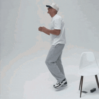 a man in a white shirt and gray pants is dancing in front of a white chair