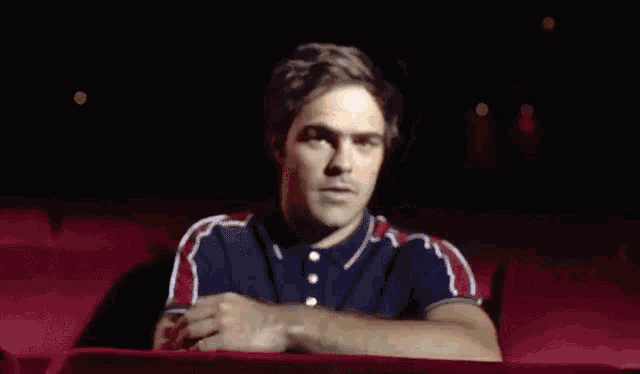 a man in a red and blue shirt leans on a red chair