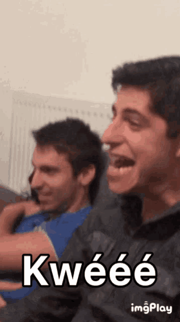 two men are sitting on a couch and one of them has the word kweeee on his face