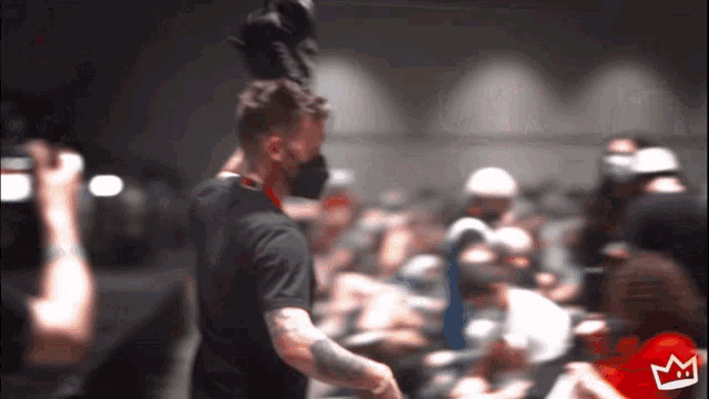a man wearing a mask stands in front of a crowd with a crown on his shirt