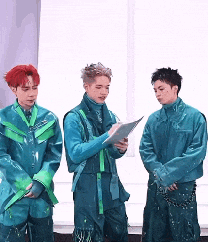a man with red hair is reading a book while two other men stand behind him