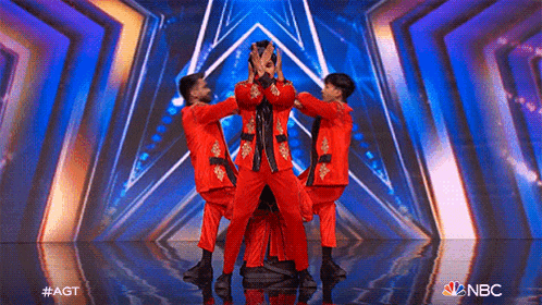 a group of men in red suits are dancing on a stage with a nbc logo in the corner