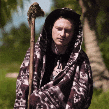 a man wearing a blanket and a hat holds a cane