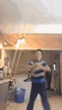 a man is dancing in a kitchen with a blue trash can in the background