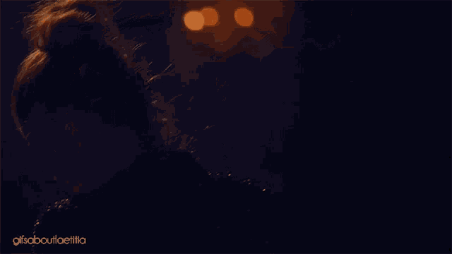 a close up of a woman 's face in a dark room with the words gifs about ellia on the bottom right