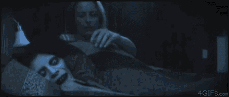 a woman is laying on a bed next to a scary face .