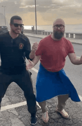 a man with a beard and glasses is dancing with another man on the street .