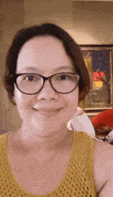 a woman wearing glasses and a yellow tank top smiles for the camera .