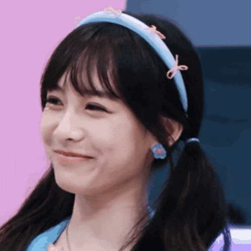 a girl with pigtails wearing a blue headband and earrings smiles