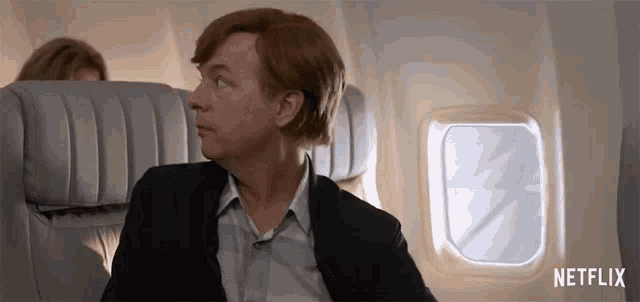 a man in a suit is sitting on an airplane with a netflix logo behind him