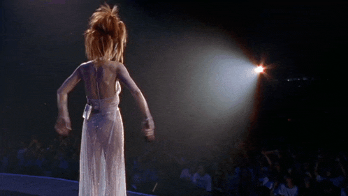 a woman in a white dress is standing on a stage in front of a crowd