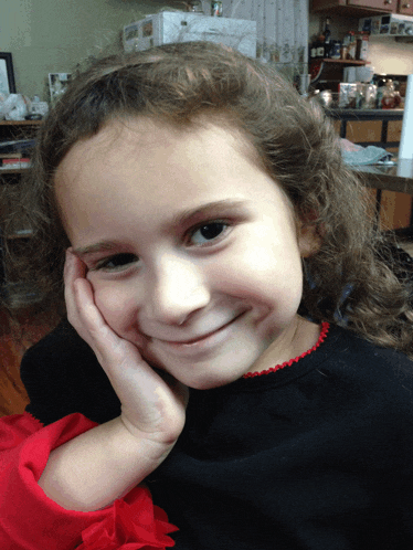 a little girl with curly hair is smiling with her hand on her chin