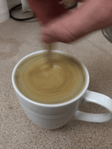 a person is stirring a cup of coffee with a silver spoon