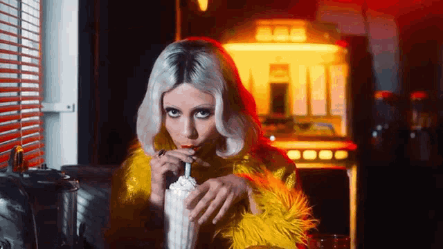a woman in a yellow fur coat drinking a milkshake through a straw .