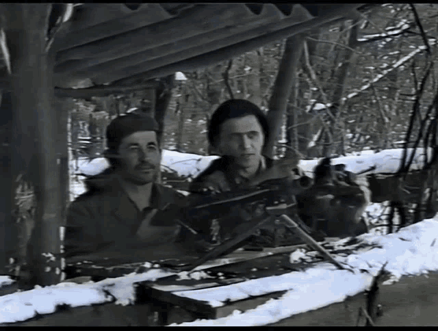 two men are sitting in the snow with a gun