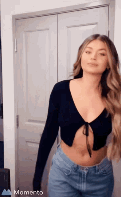 a woman in a black crop top and blue shorts is standing in front of a door with the word momento on the bottom