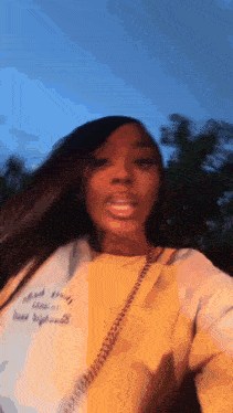 a woman in a yellow sweater is taking a selfie with her phone .