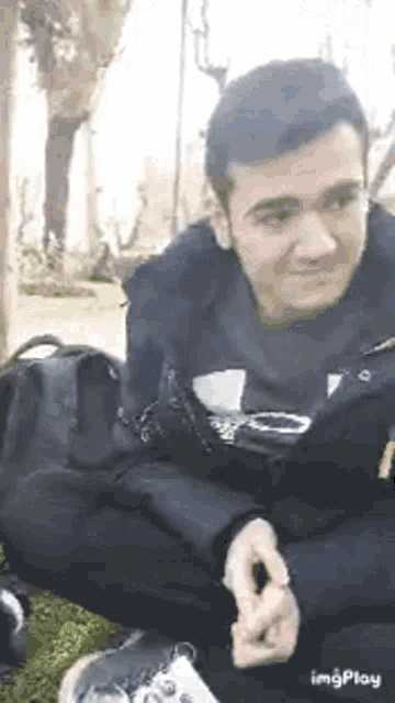 a man is sitting on the grass with his legs crossed and looking at his phone .