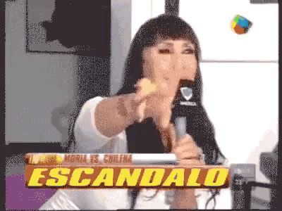a woman holds a microphone in front of a sign that reads escandalo