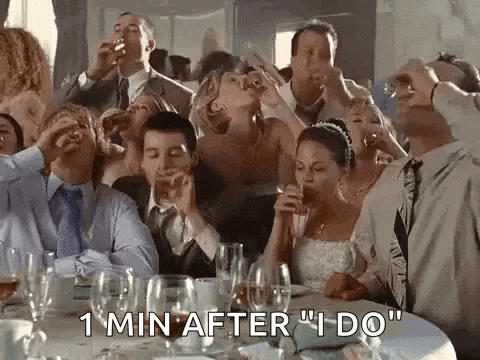 a group of people are sitting at a table drinking wine and toasting at a wedding reception .