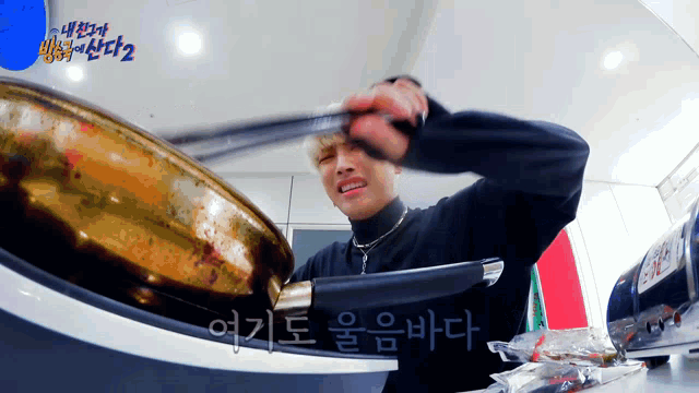 a man in a black sweater is holding a frying pan in front of a sign that says " 2 "