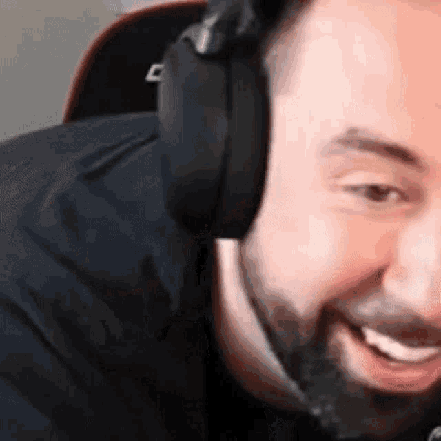 a man with a beard is wearing headphones and smiling while playing a video game .