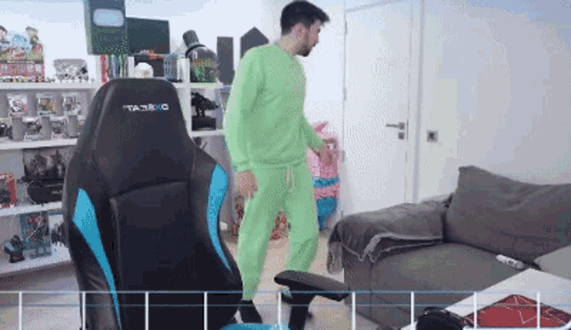 a man in green pajamas is standing in front of a gaming chair that says ta3bro on it .