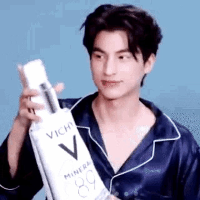 a man in a blue pajama shirt is holding a bottle of vichy lotion .