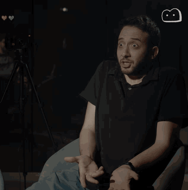 a man in a black shirt is sitting on a couch with the words gel-mi-yo- written above him