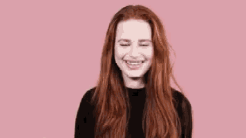 a woman with long red hair is wearing a black shirt and smiling .