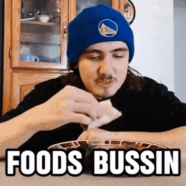 a man wearing a golden state warriors beanie is eating a sandwich