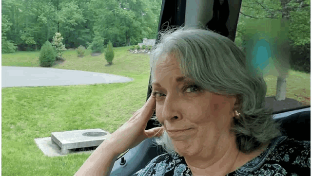 a woman with gray hair is sitting in a car with her hand on her head