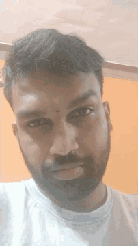 a man with a beard wearing a white shirt looks down at the camera
