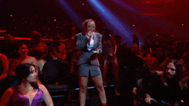a woman is singing into a microphone in front of a crowd of people