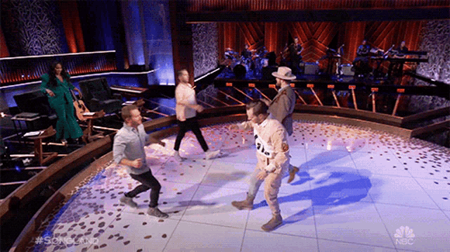 a group of people are dancing on a stage in front of a nbc sign
