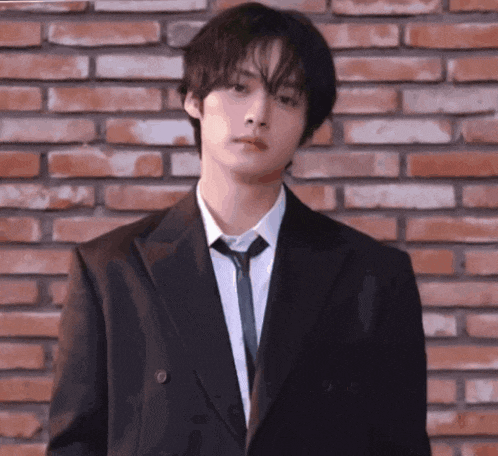 a young man is wearing a suit and tie and standing in front of a brick wall .