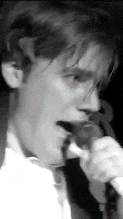 a man is singing into a microphone while wearing a white shirt and tie .