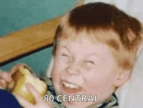 a young boy is making a funny face while holding a banana and the words 80 central are visible behind him .