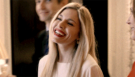 a woman with long blonde hair and red lipstick is smiling while standing next to a man and a woman .