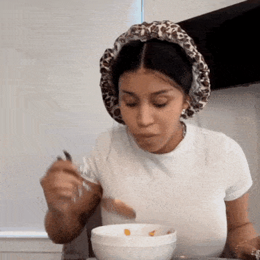 a woman wearing a leopard print hat is eating cereal from a bowl with a spoon