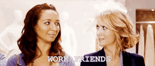 two women are standing next to each other and the words work friends are on the screen behind them .